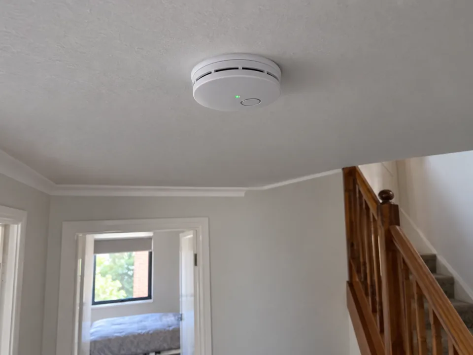 Smoke alarm on a white ceiling above a stairwell in a light-painted home in Epping