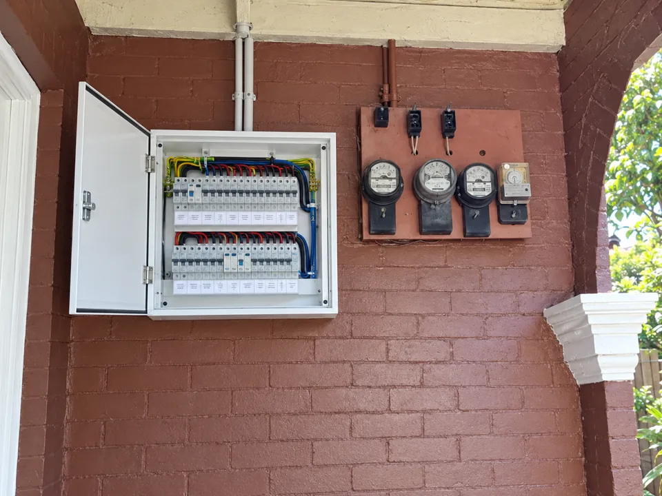 Open electrical switchboard and meter panel on a red brick exterior wall in Beecroft